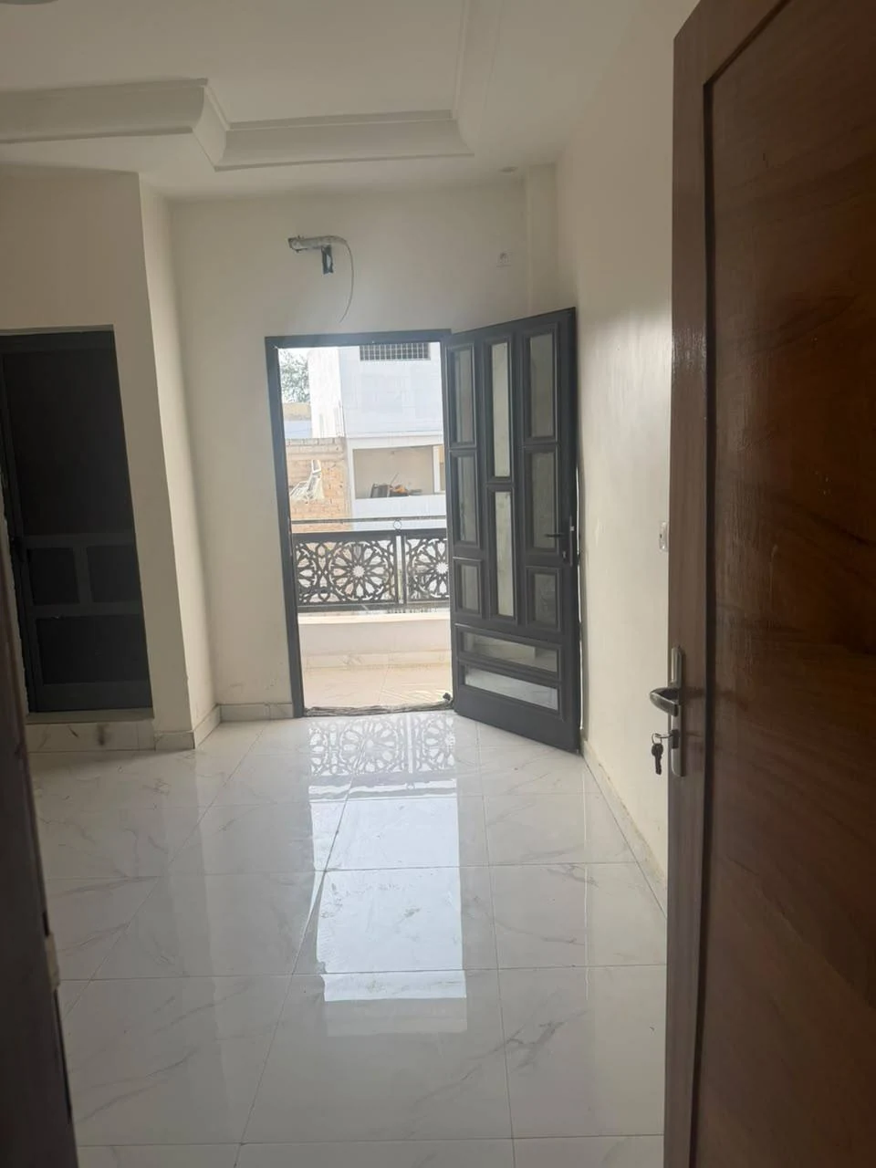 Intérieur du studio non meublé avec porte ouverte vers un balcon et sol carrelé clair